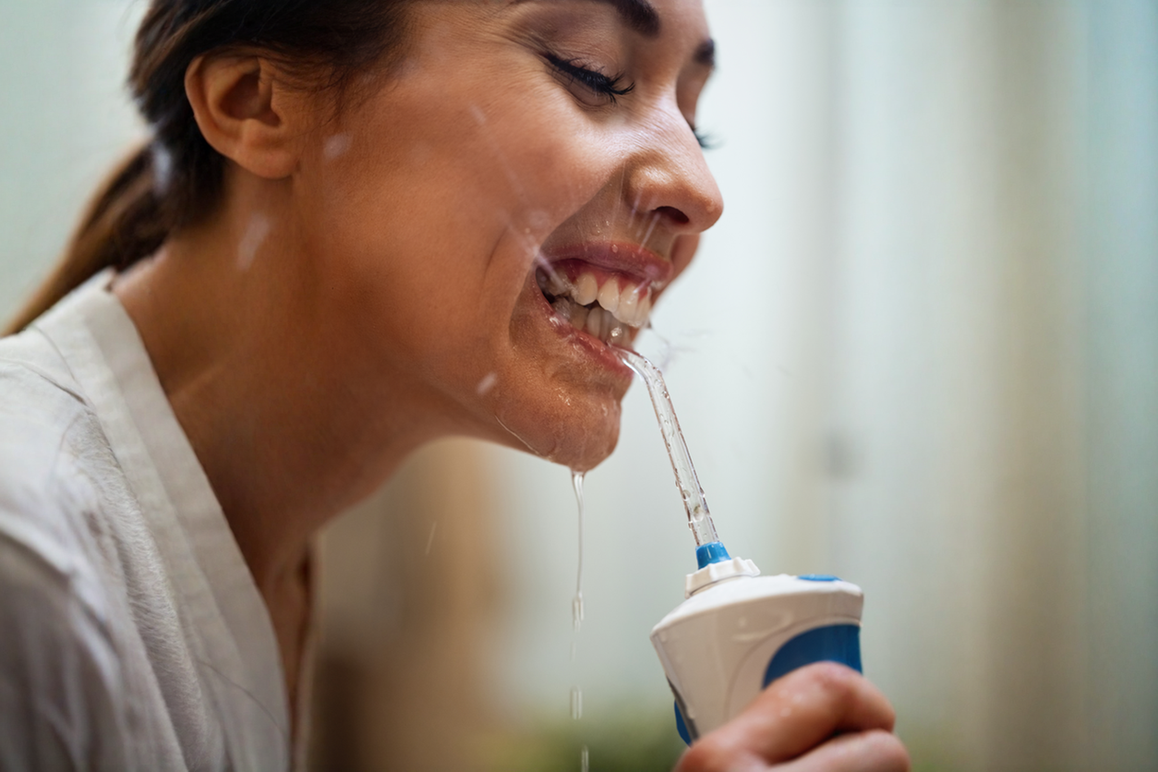 امرأة تنظف أسنانها باستخدام جهاز خيط الاسنان المائي – فوائد خيط الاسنان المائي لصحة الفم