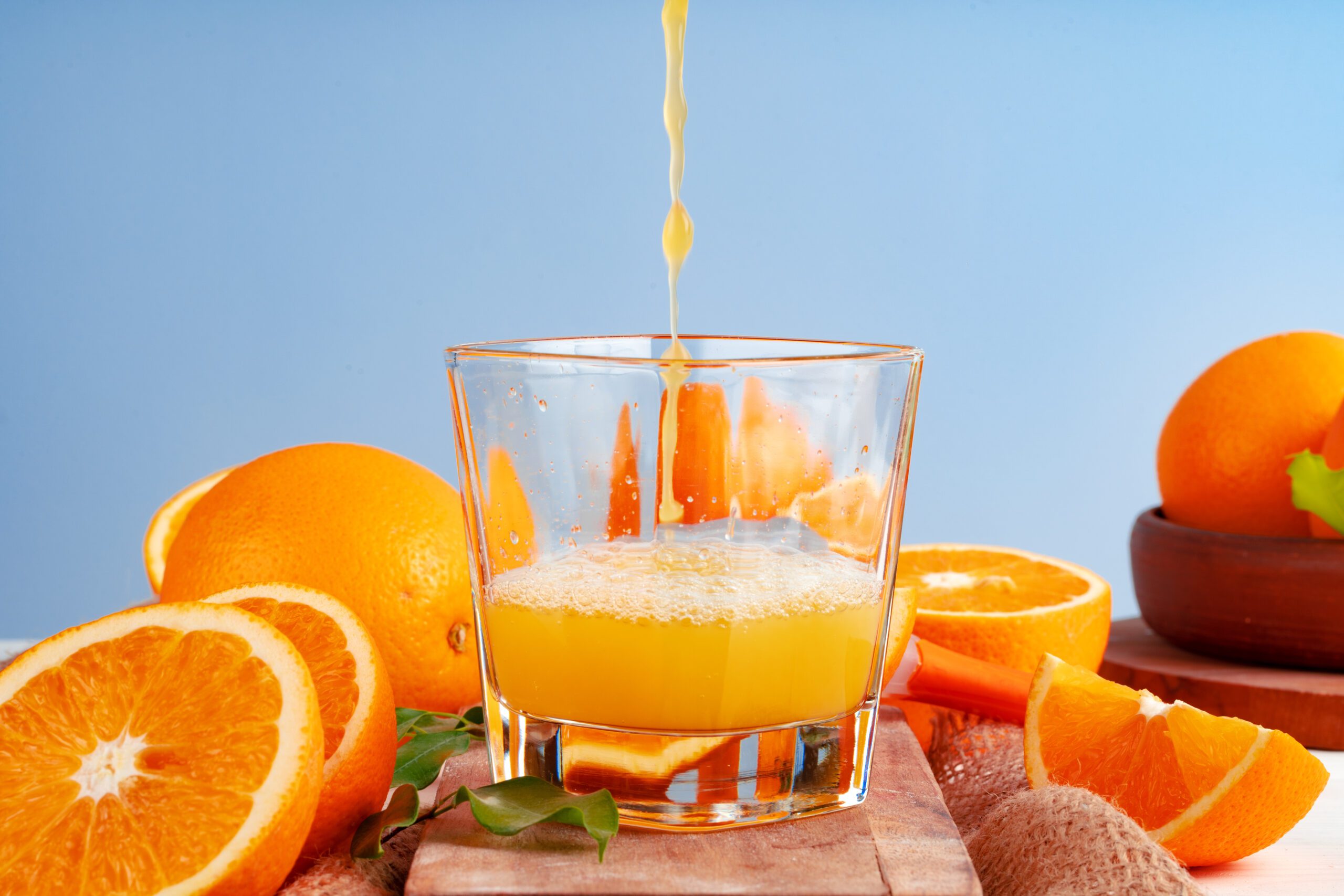 كوب عصير برتقال طازج يُسكب مباشرة مع برتقال مقطع على الطاولة