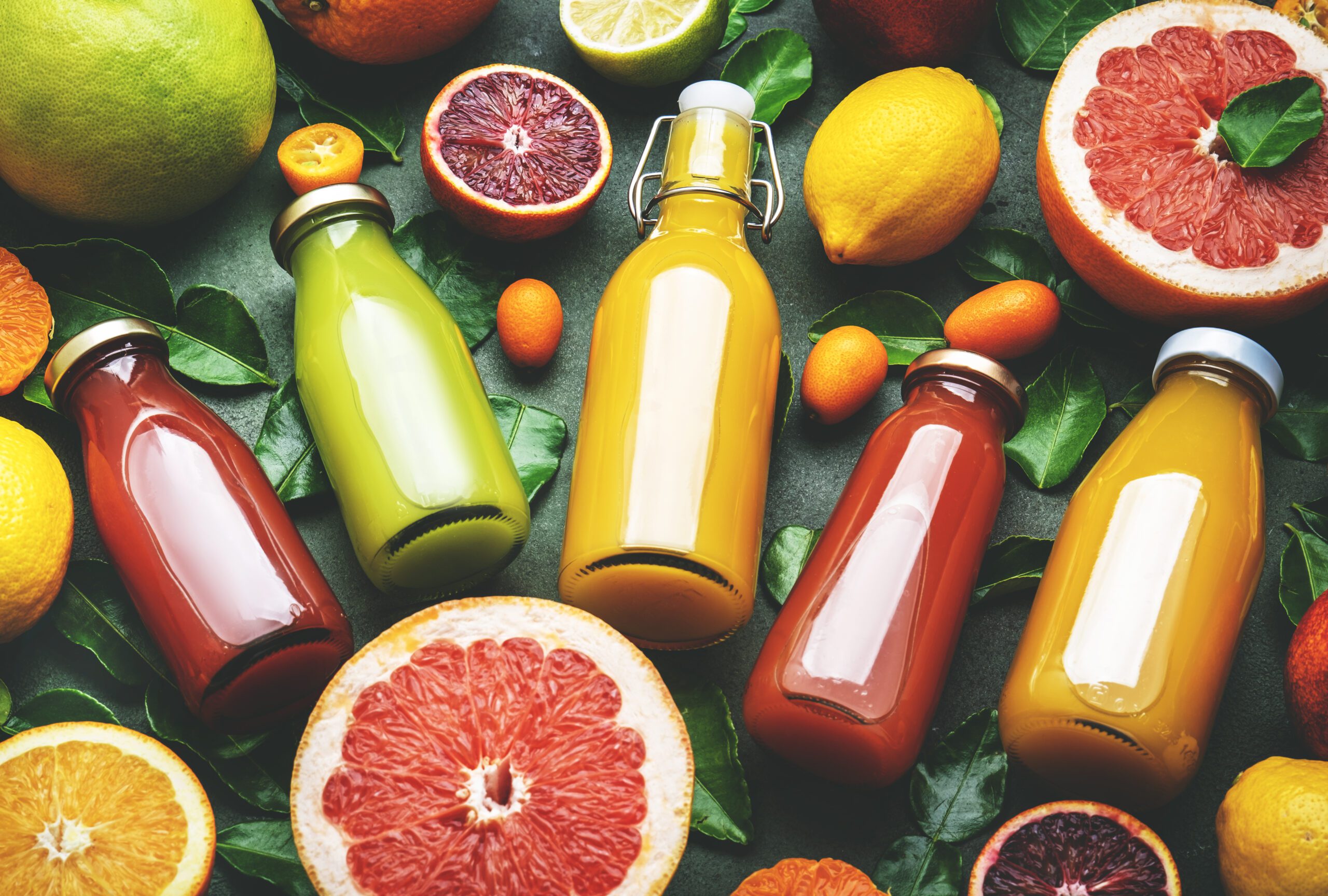 زجاجات عصير فواكه طبيعية متنوعة بألوان مختلفة مع شرائح جريب فروت وبرتقال وليمون